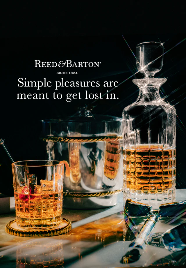 Crystal glasses and decanter with a drink, featuring Reed & Barton branding and text.